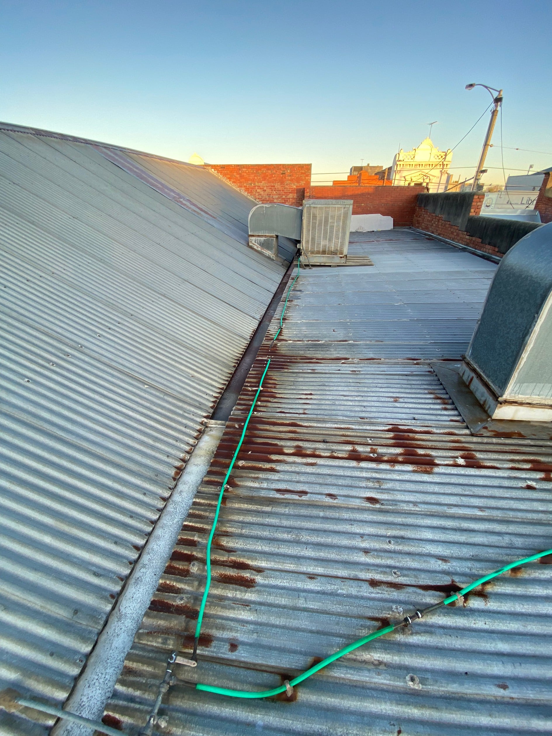 Blue and silver metallic corrugated rooftop with brown corrosion stains. the horizon has orange brick buildings and a blue skyline.