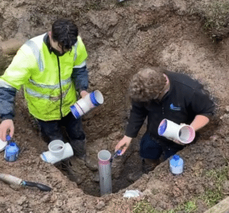An aerial view of two plumbers repairing pipes in a trench.