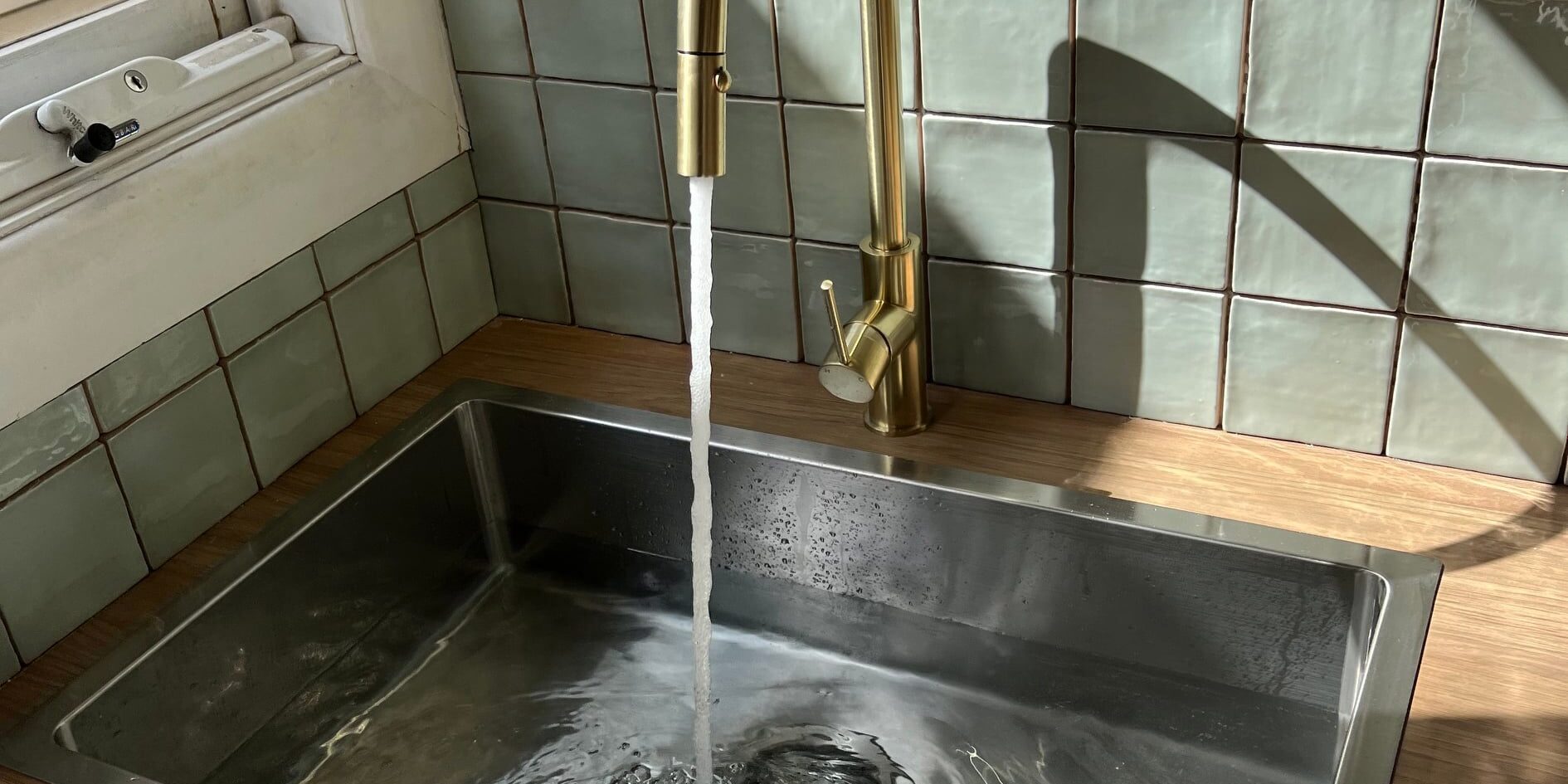 Gold Tap Faucet Running Water into a chrome sink that is filled with water. Blockages Tiles