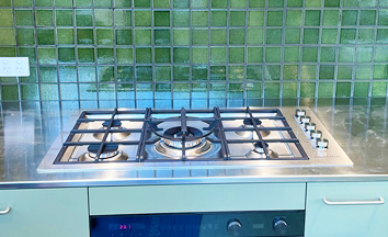 a new clean gas cooktop on a green bench. there are medium sized shiny green tiles behind it