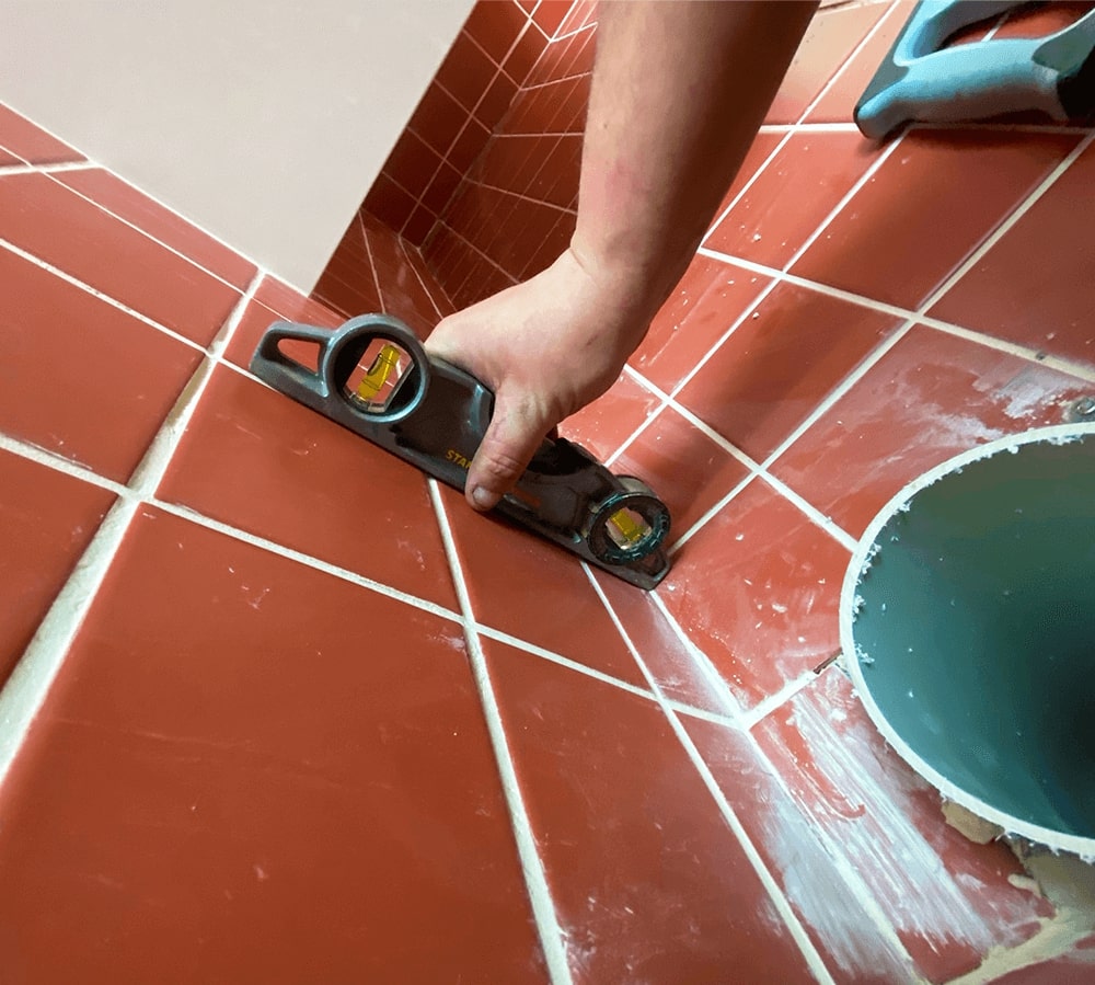 hand on orange bathroom tiles applying grout using a long spatula