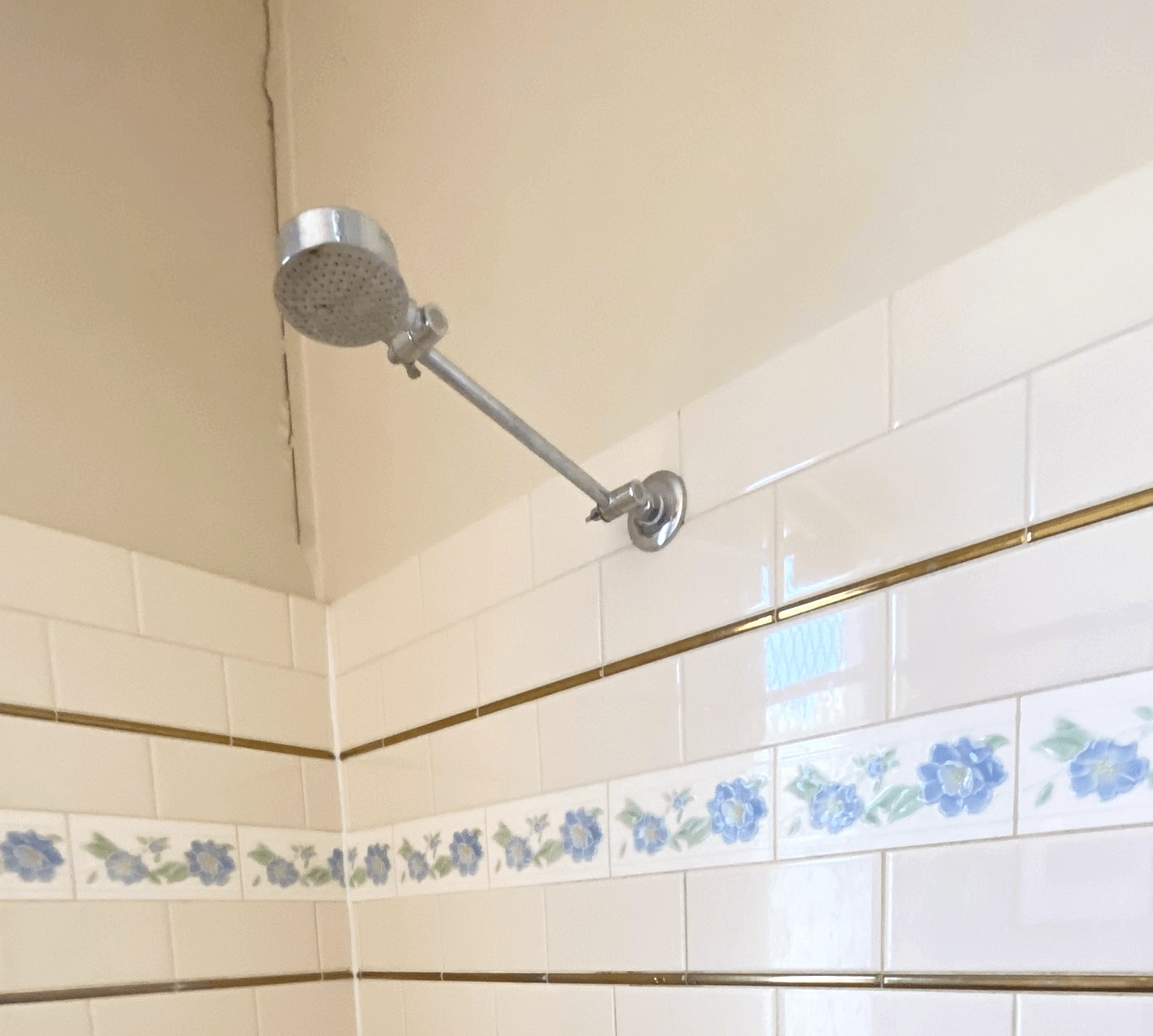 an silver showerhead potruding from a cream square tiled wall. two long lines appear between the tiles as decoration